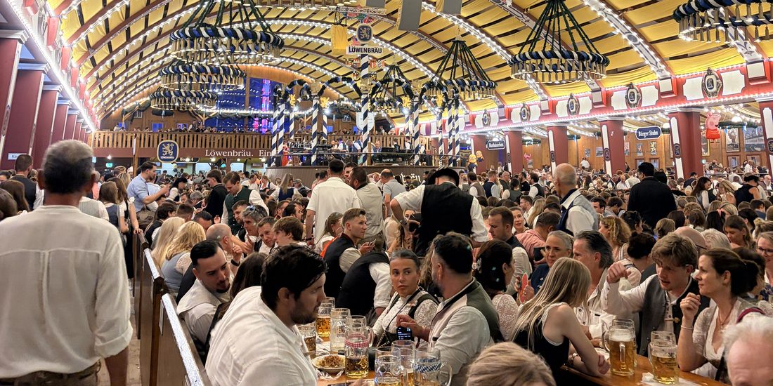 Inside a packed Oktoberfest tent — chandeliers of hops, steins on every table