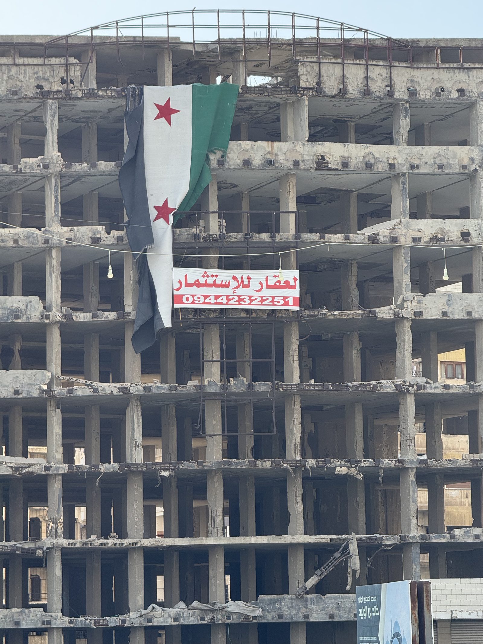 A war-damaged multi-storey building in Syria hung with the Syrian independence flag